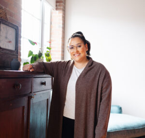 Picture of Jess smiling on camera standing next to a brown drawer. | The Listings Lab | How to Generate Leads for Real Estate Online