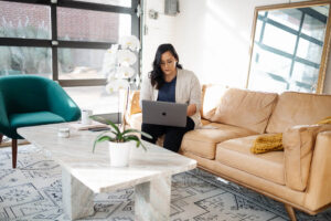 Picture of Jess Using Her Computer Sitting on a Mustard Couch | Why Real Estate Agents Fail | The Listings Lab